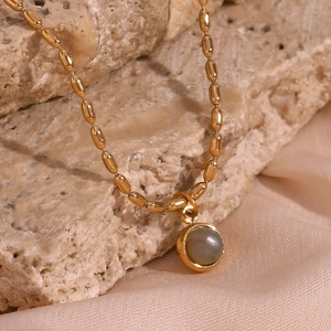 Macro shot of 18K gold beaded chain necklace with round gray gemstone on silk and stone