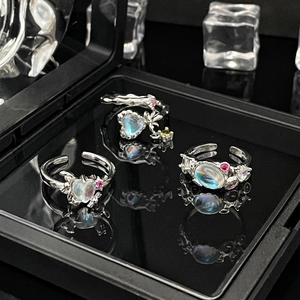 Three silver moonstone rings with heart and bow designs on a black mirror base