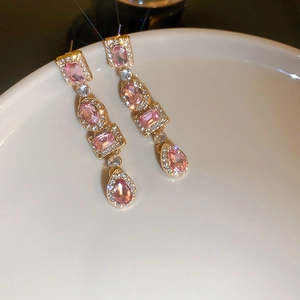 Detail of luxury gold earrings featuring pink gemstones and crystal pavé on ceramic