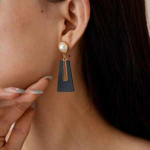 Detail of elegant gold hollow geometric earrings with white pearl and black resin pendant