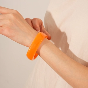 Close-up of a translucent orange resin geometric square bangle on a woman's wrist