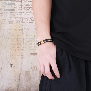 Détail d'un bracelet en cuir noir tressé avec un clou pyramidal doré sur un poignet masculin