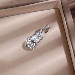 Détail d'une broche violon argentée avec strass clairs dans un coffret à bijoux beige