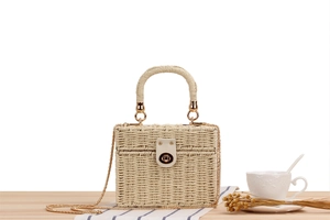Close-up of woven straw box bag with golden metal chain and twist lock detail