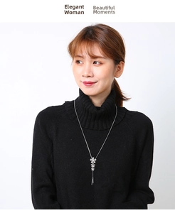 Elegant silver flower necklace with metallic tassels worn on black turtleneck sweater