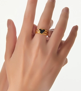Détail d'une bague multicouche dorée avec un cœur en émail noir portée au doigt
