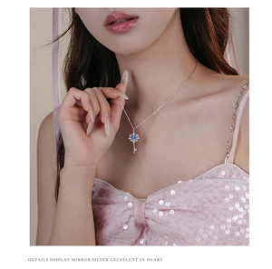 Close-up of a S925 sterling silver heart-shaped key necklace with a blue gemstone on a model