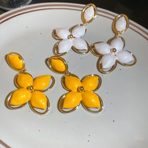 Vue détaillée de boucles d'oreilles trèfle jaune et blanc en émail sur un plat en céramique