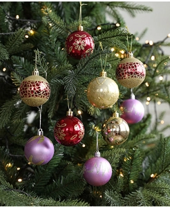 Detail of glitter-patterned Christmas baubles in red and gold hanging on a pine tree