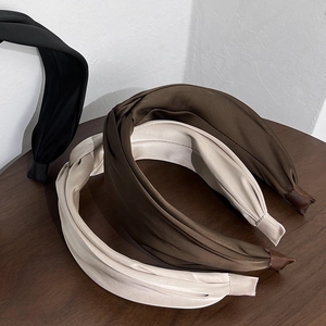 Three elegant wide padded satin headbands in black, brown, and beige on wooden surface