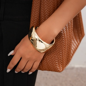 Close-up of a wide polished gold metal cuff bracelet with a minimalist wavy design