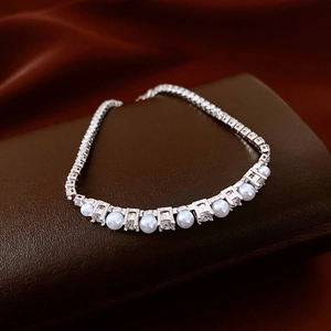 Macro shot of zircon pearl chain bracelet on luxury leather and burgundy silk background