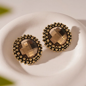 Vintage gold-toned round flower stud earrings with amber rhinestones on a ceramic tray