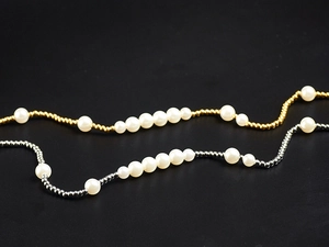 Detail view of gold and silver metal beads mixed with round white pearls on a dark background