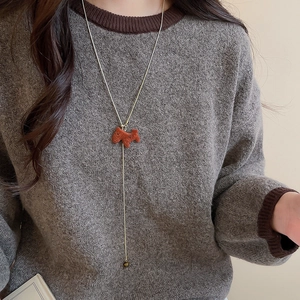 Close-up of a Y-shaped gold necklace with a brown flocked pony pendant on a gray sweater