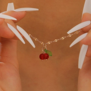 Macro shot of gold cherry pendant necklace with red crystal beads and green leaf detail