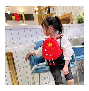 Side view of a red cartoon dinosaur toddler backpack worn by a little girl