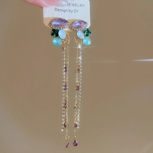 Detail of luxury long tassel earrings with multicolored crystals and gold leaf accents
