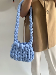 Close-up of a blue chunky knit shoulder bag showing thick woven cord texture on a model