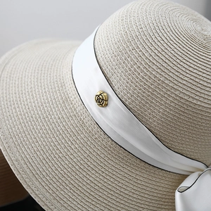 Oat beige straw sun hat with elegant white bow ribbon and golden camellia detail