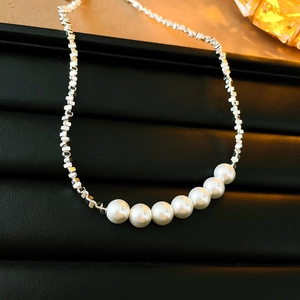 Détail d'une chaîne en perles métalliques argentées avec sept perles baroques blanches