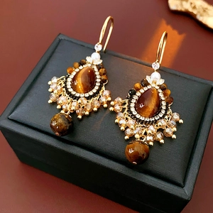 Close-up of vintage gold earrings with amber tiger eye stone and crystal beads on a box