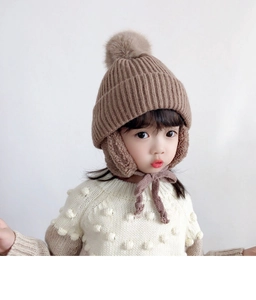Close-up of khaki knitted winter earflap hat with fluffy pom-pom and windproof straps