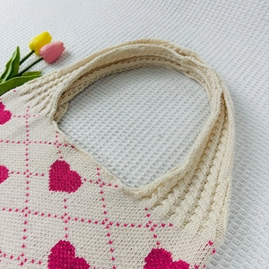 Detailed close-up of a beige knitted tote bag with pink heart patterns and grid texture
