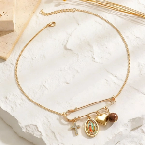 Close-up of gold paperclip necklace with cross, Maria medal and heart charms on rock