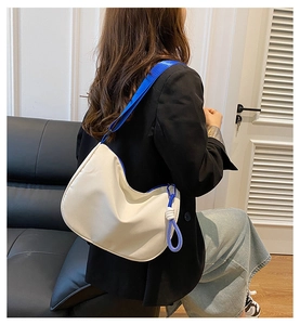 White nylon tote bag with blue fabric shoulder strap and knot charm in a lifestyle setting