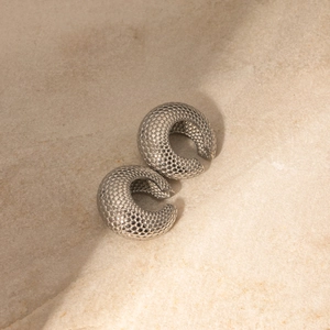 Macro shot of silver fish scale textured earrings on beige stone texture background