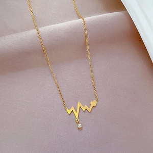 Macro detail of gold heartbeat necklace with a small heart and crystal on soft fabric