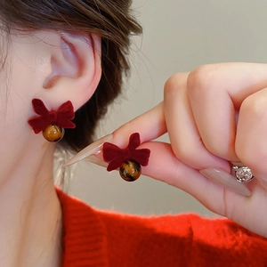 Detail of red velvet bow earrings with glossy brown beads shown on a model