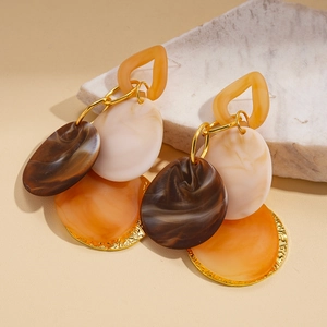 Detail of geometric acrylic earrings with tortoise and marble patterns on white stone