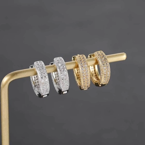 Macro shot of gold and silver pave set huggie hoop earrings on a metal display stand