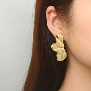 Golden irregular pleated flower earrings in polished metal on female model's ear