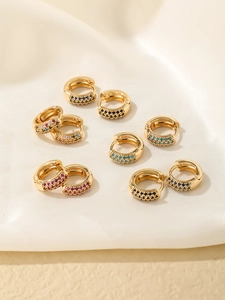 Détail de boucles d'oreilles huggies dorées avec zircons colorés sur tissu en soie blanche