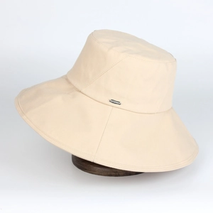Detail of beige bucket hat featuring wide brim and elegant silver rectangular metal plaque