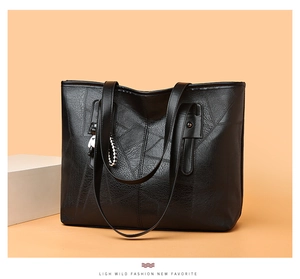Macro detail of large black tote bag featuring stitched patchwork leather and woven charm