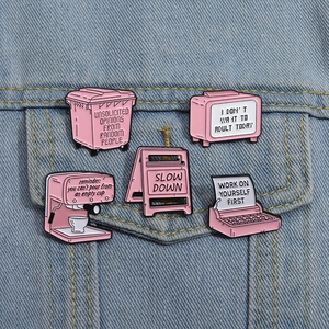 Pink enamel pins featuring coffee machine and typewriter designs on a denim jacket pocket