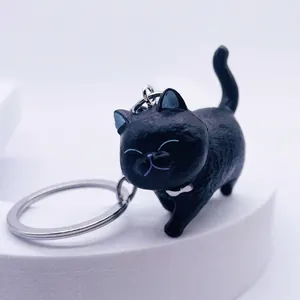 Close-up of black resin cat keychain with silver metal ring on white stand