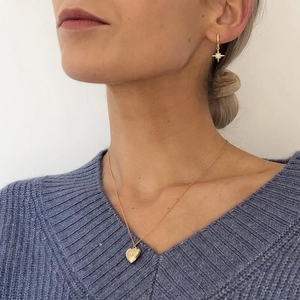 Close-up of gold heart locket necklace and star stud earrings on a female model