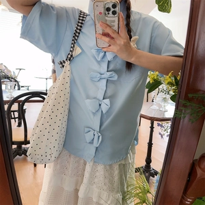 Close-up of a light blue short-sleeved shirt featuring four decorative bow tie closures