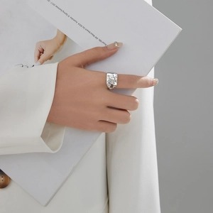 Close-up of wide silver lava ring with irregular texture worn by a model holding a magazine