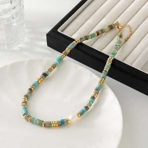 Natural jasper beaded necklace with a white teardrop pearl and golden accents on a white plate