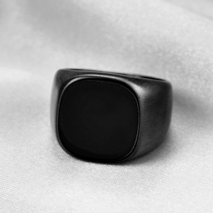 Detail of matte black brushed stainless steel signet ring on grey silk fabric