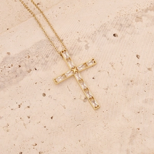 Detailed close-up of 18K gold-plated cross pendant with sparkling zircon on a stone surface