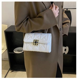 Detail view of white quilted leather bag with black gem clasp and gold chain strap