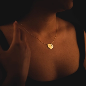 Gold sun and moon pendant necklace with face design on female model in dark lighting