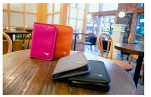 Detailed set of four travel passport wallets in pink, orange, grey, and navy with gold plane logo